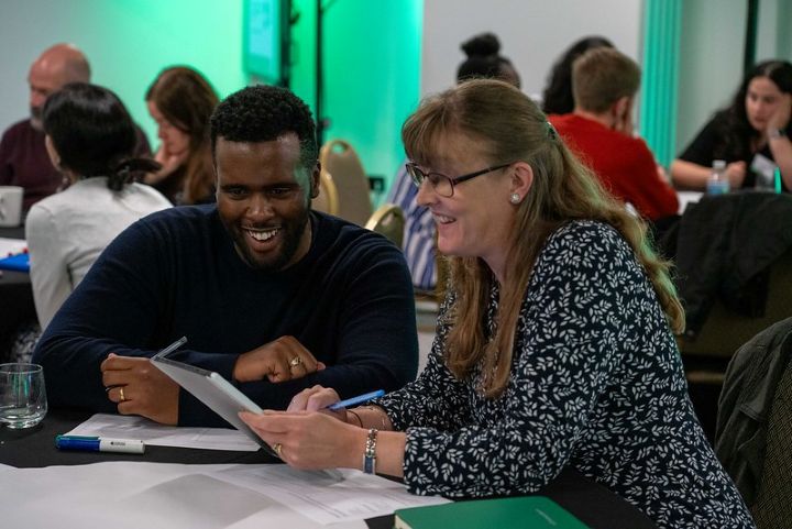 A man and a woman sat at a table discussing a topic on a piece of paper. Photograph from VitaeCon2023.