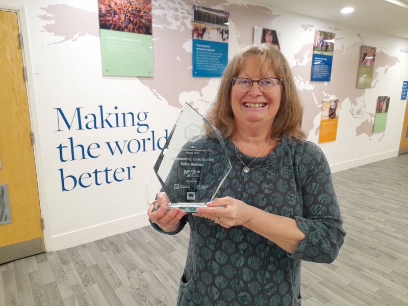 Photograph by Jon Nurse of Julie Reeves with her ICE Award standing in front of a wall that says 'Making the world better'.