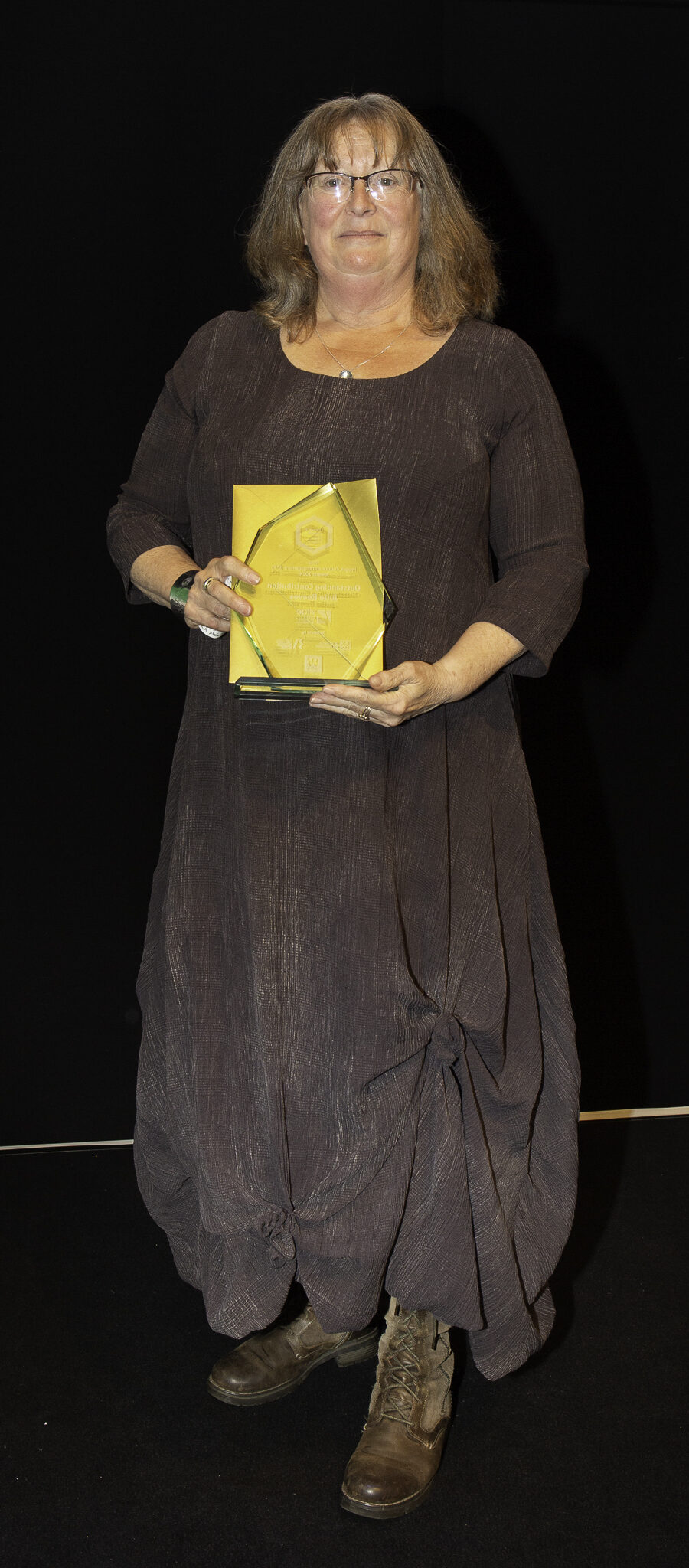 A woman holding a trophy in front of a black background.