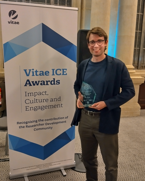 Tom Webb holding his ICE Award in front of the ICE banner.