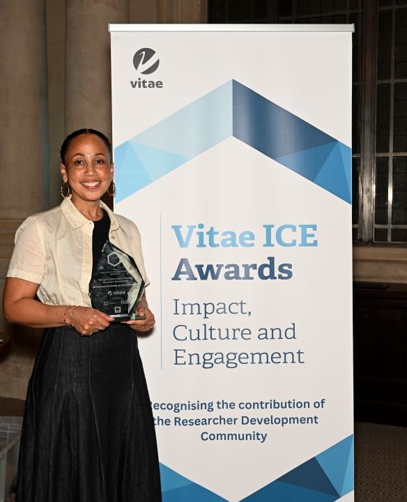 Kate Theophilus holding her ICE Award trophy in front of the ICE Award banner,