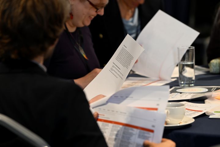People reading pieces of paper, with a close up view of the paper.  Image from #VitaeCon2025 by Andrew Callaghan.