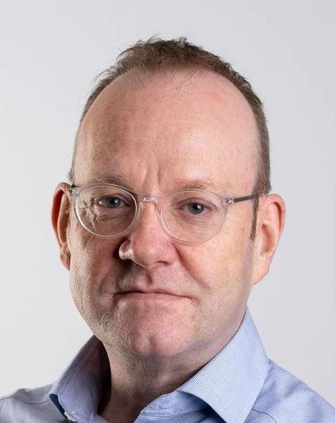 A man wearing transparent glasses in front of a blank background.