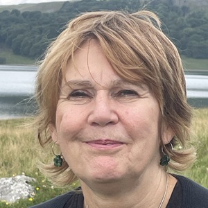 A white woman with short cropped hair with a natural landscape behind her.