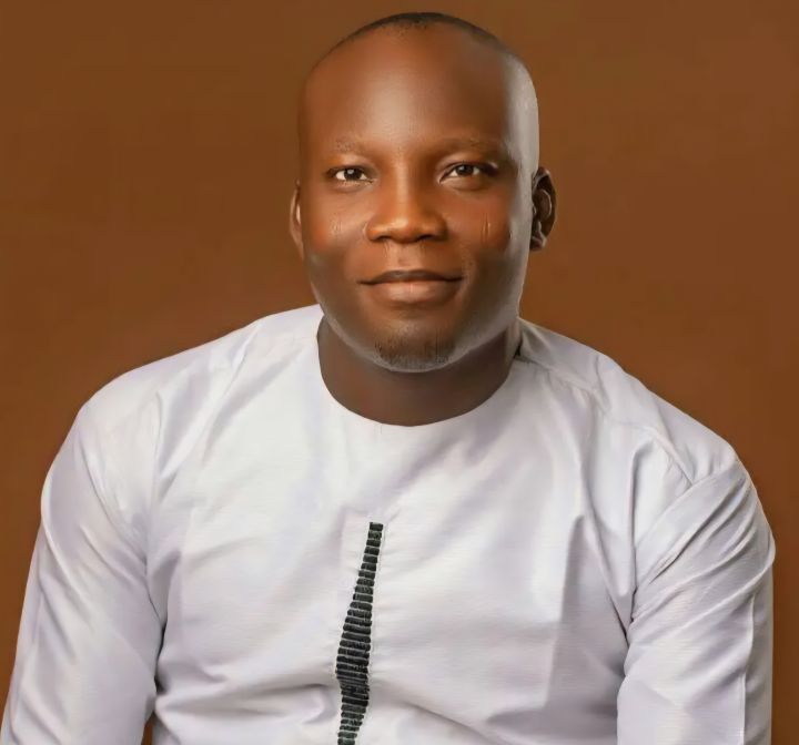 A man of colour wearing a white shirt in front of a brown background.
