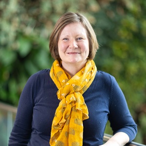 A white woman with short cropped hair wearing a bright yellow scarf.