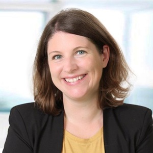 A white woman with brown hair and smiling wearing a dark jacket.